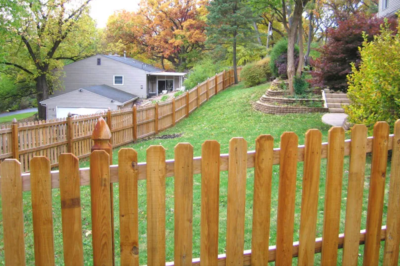Close up of wood fence enclosing a lawn with a house and fall-colored trees in the background