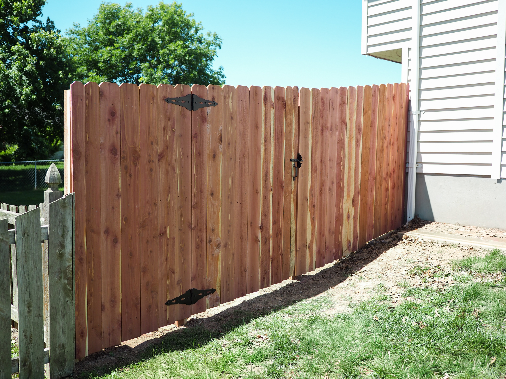 Wood gate attached to a fence on the side of a house.
